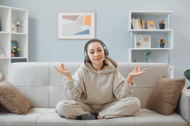 Photo of a young woman at home sitting o a couch with headphones