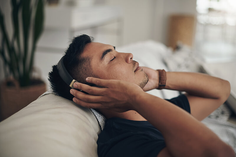A photo of a man relaxing on the sofa at home hearing music on headphones