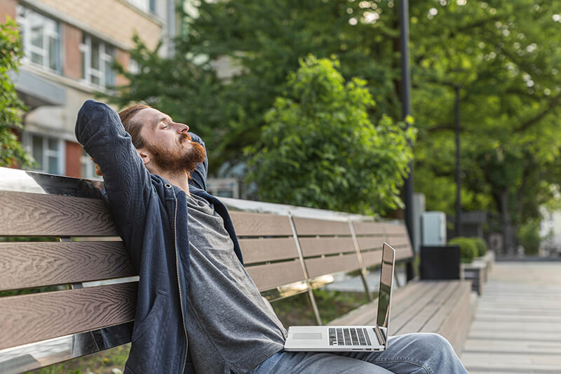 Photo of a man sitting on a bench with a laptop