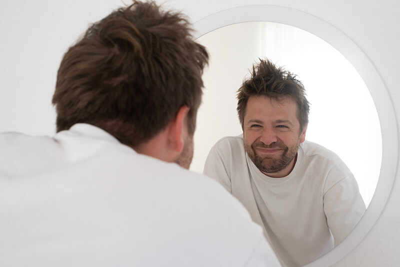A photo of a tired, mature man looking at a mirror
