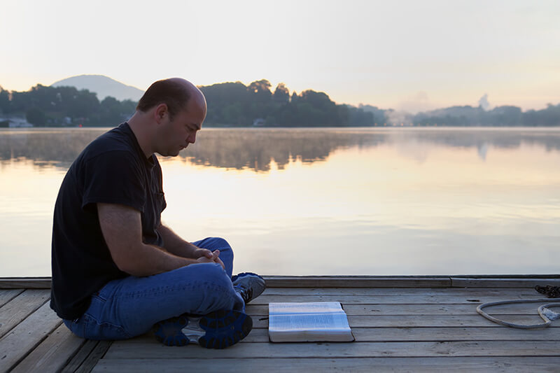 A photo of a man reading a book by a lake