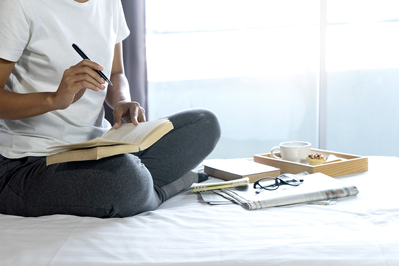 A photo of a woman sitting on a sofa writing in a journal