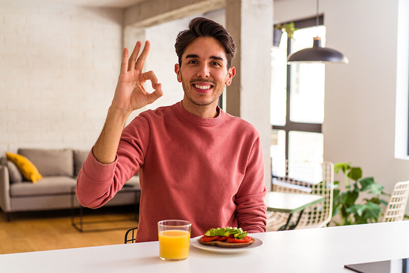 A photo of a young man looking very happy doing the ok sign with a glass of orange juice