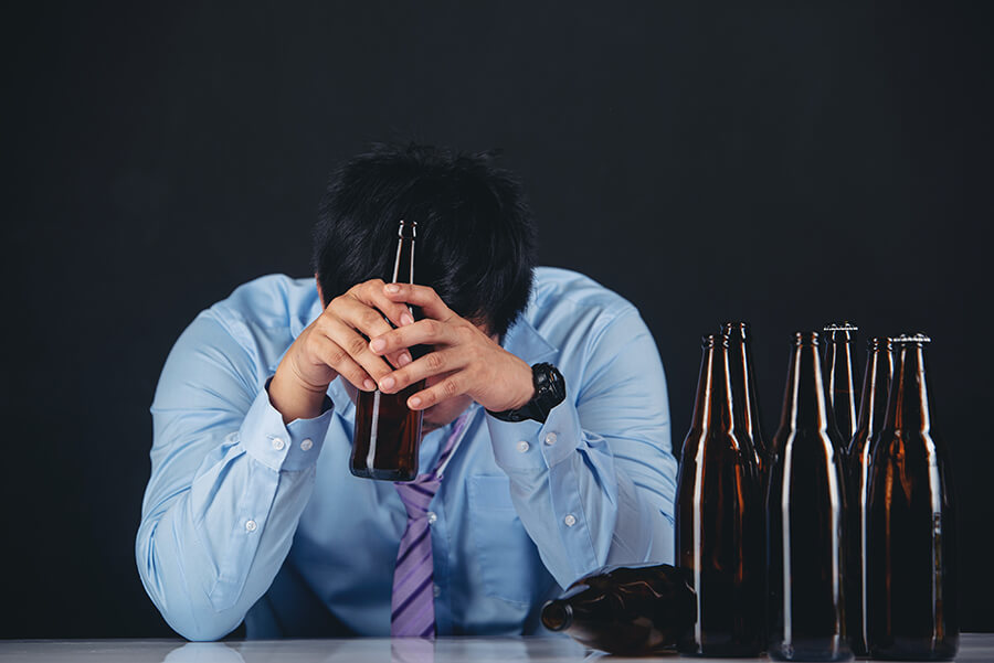 Photo of a man with his head between his hands with several empty beer bottles in front of him