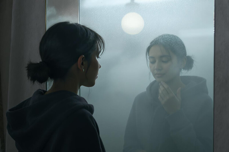 A photo of a woman in front of a mirror with her eyes closed