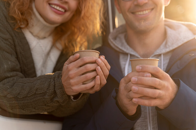 Photo of a couple smiling while holding takeaway cups of tea
