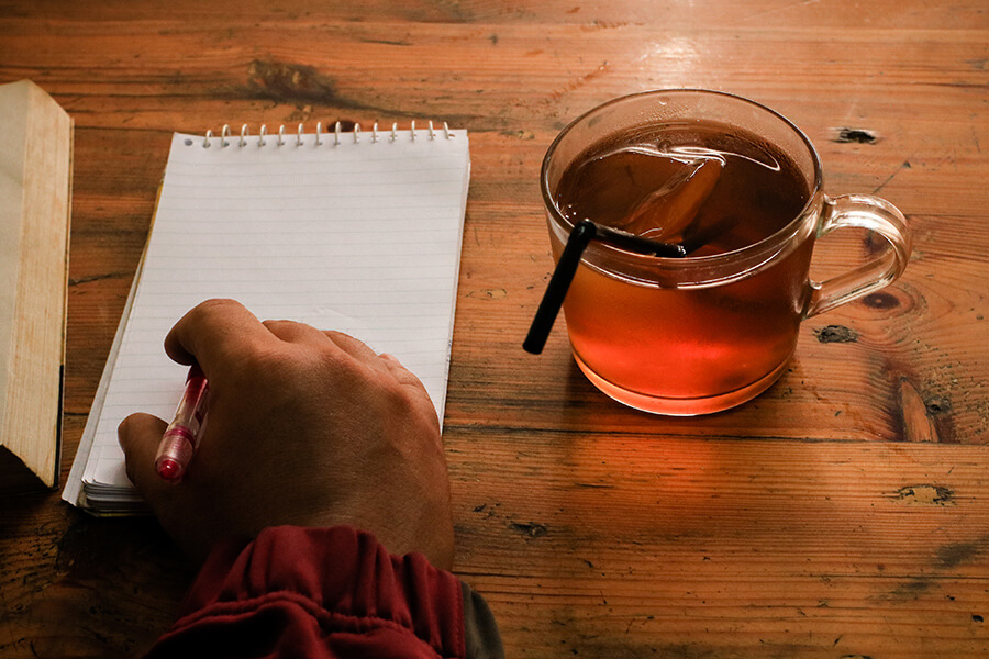 A photo of a man writing in a block with a glass of tea