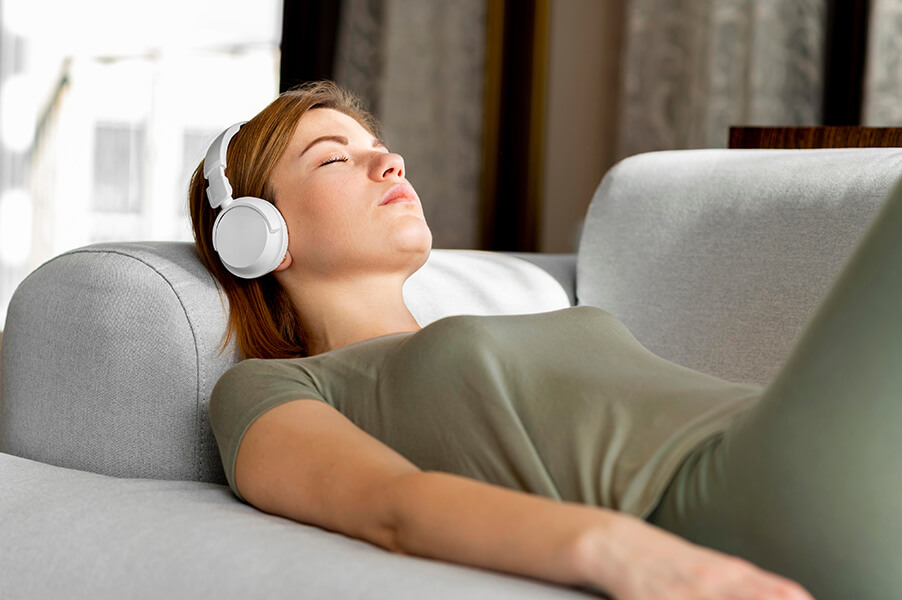 A photo of a woman lying down listening to headphones with her eyes closed