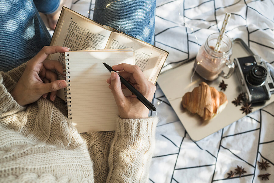 A photo of a woman writing in a journal next to a tray with breakfast