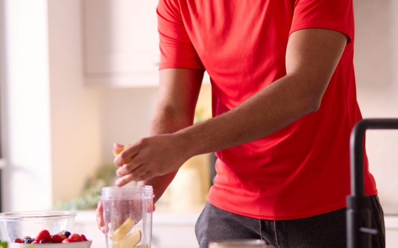 Man In Kitchen At Home Wearing Fitness Clothing Blending Fresh Ingredients For Healthy Drink