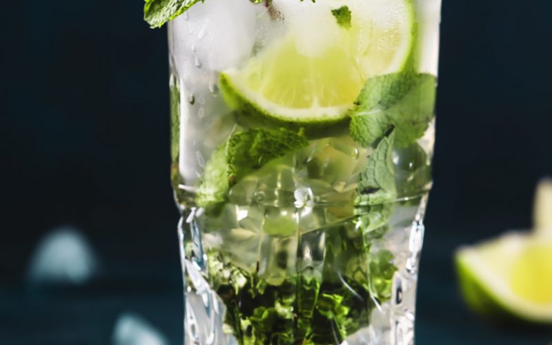 Mojito cocktail or mocktail with lime, mint, and ice in glass on blue background. Summer cold alcoholic non-alcoholic drink,  beverage and cocktail. Copy space
